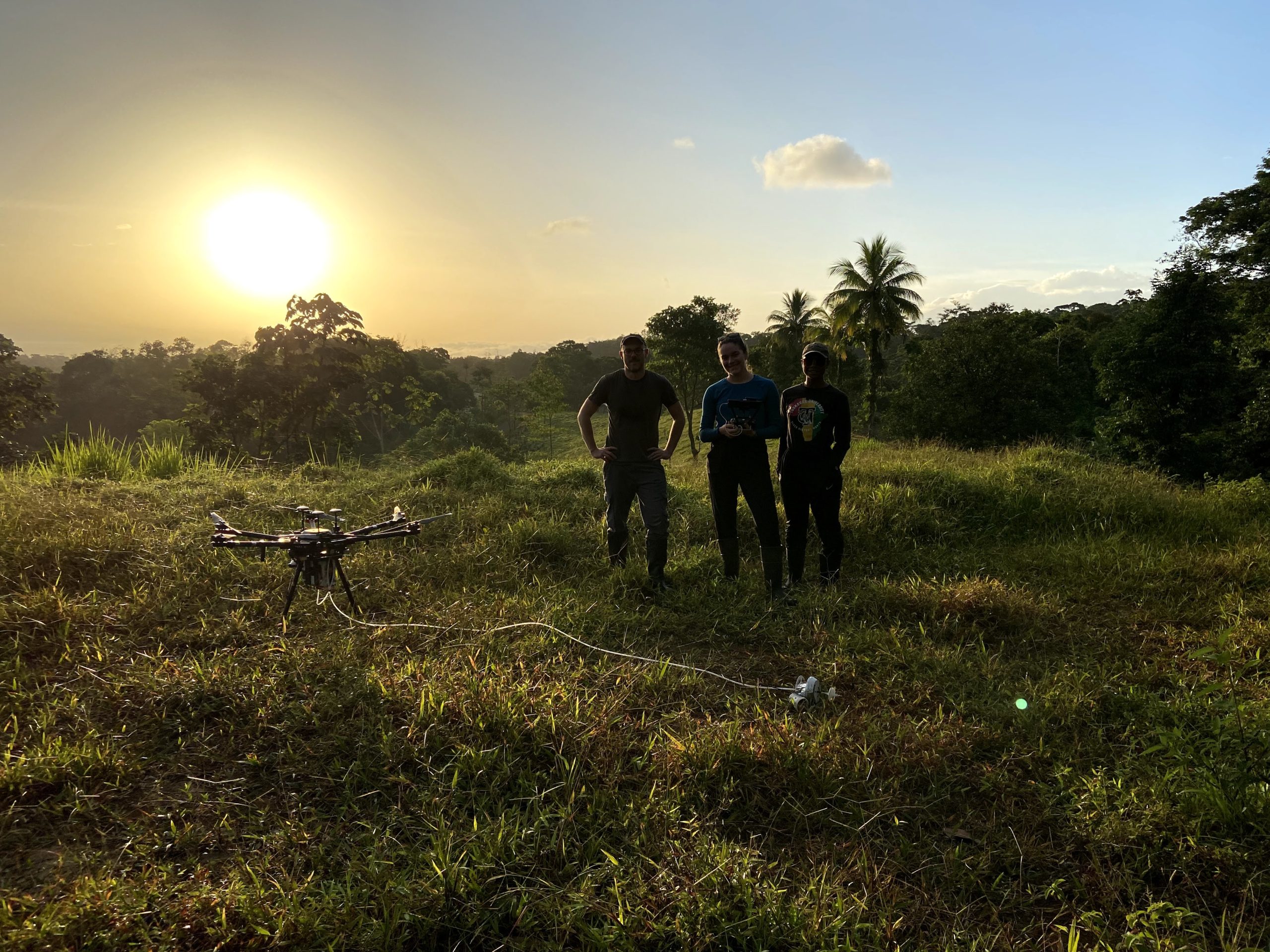 Drone and project researchers shown as sun rises over tropical forest.
